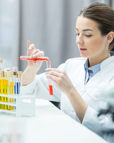 Young female scientist in lab coat making experiment in chemical lab